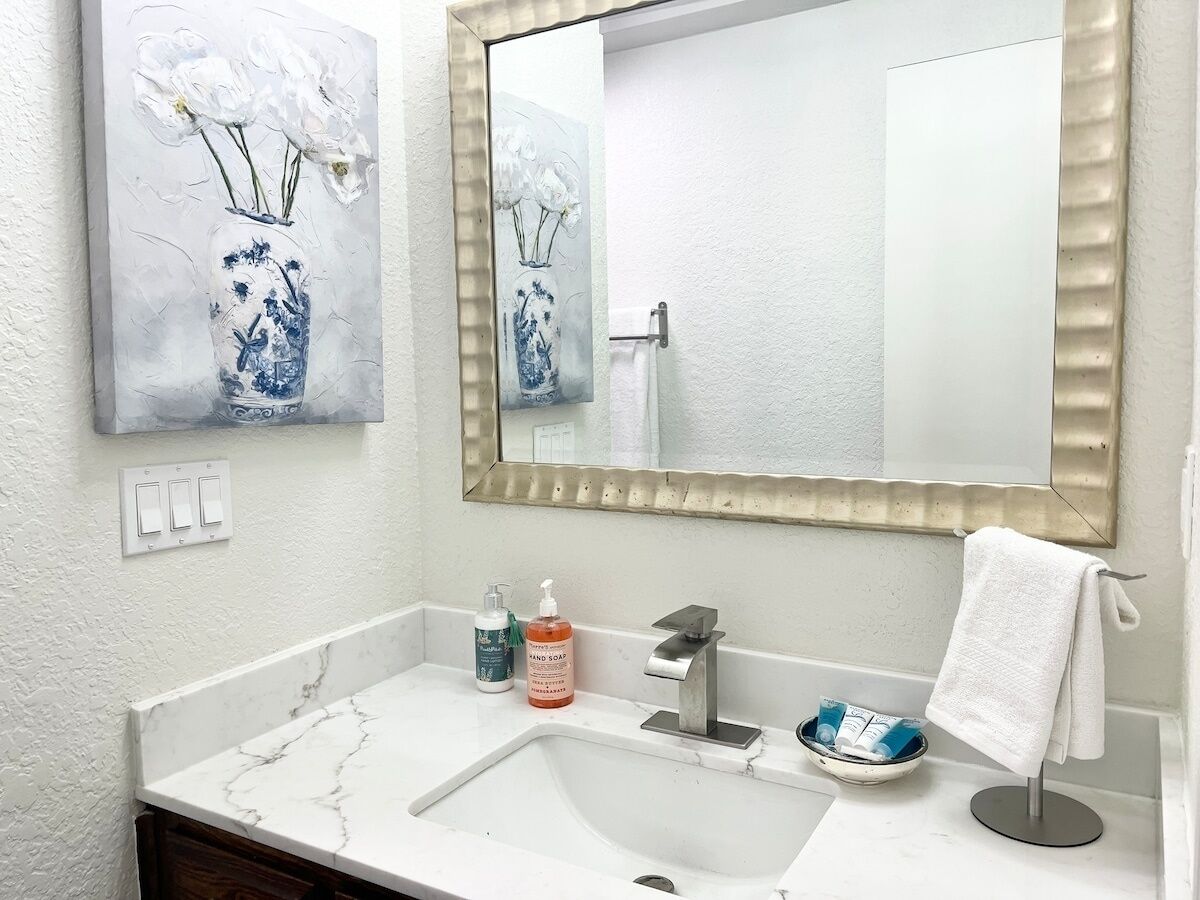 A bathroom with a white marble sink, a large mirror, and two wall-mounted paintings of flowers.