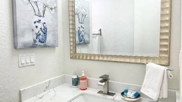 A bathroom with a white marble sink, a large mirror, and two wall-mounted paintings of flowers.