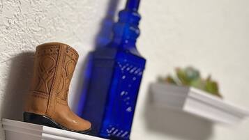 Una bota vaquera de madera y una botella azul sobre estantes blancos frente a una pared con textura.