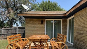 Un patio con una mesa de madera y bancos, un muro de ladrillo y una puerta corrediza de vidrio.