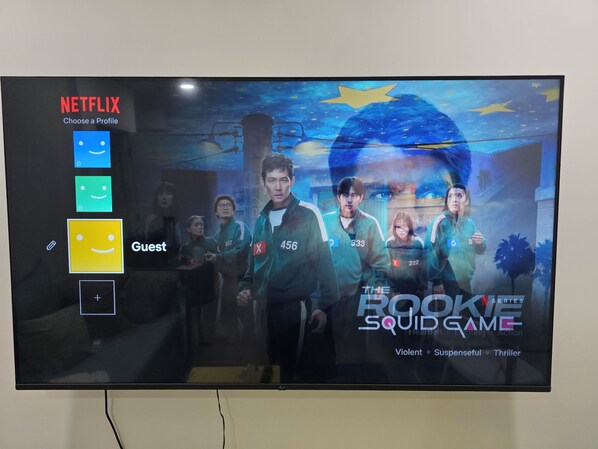 Una pantalla de televisión muestra una interfaz de Netflix con una selección de perfiles y un cartel de la película 'El Juego del Calamar'.