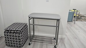 Une petite pièce avec un chariot en métal, un pouf à motifs et une table jaune avec une chaise.