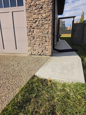 A residential driveway with a stone wall, a concrete pathway, and a wooden fence.
