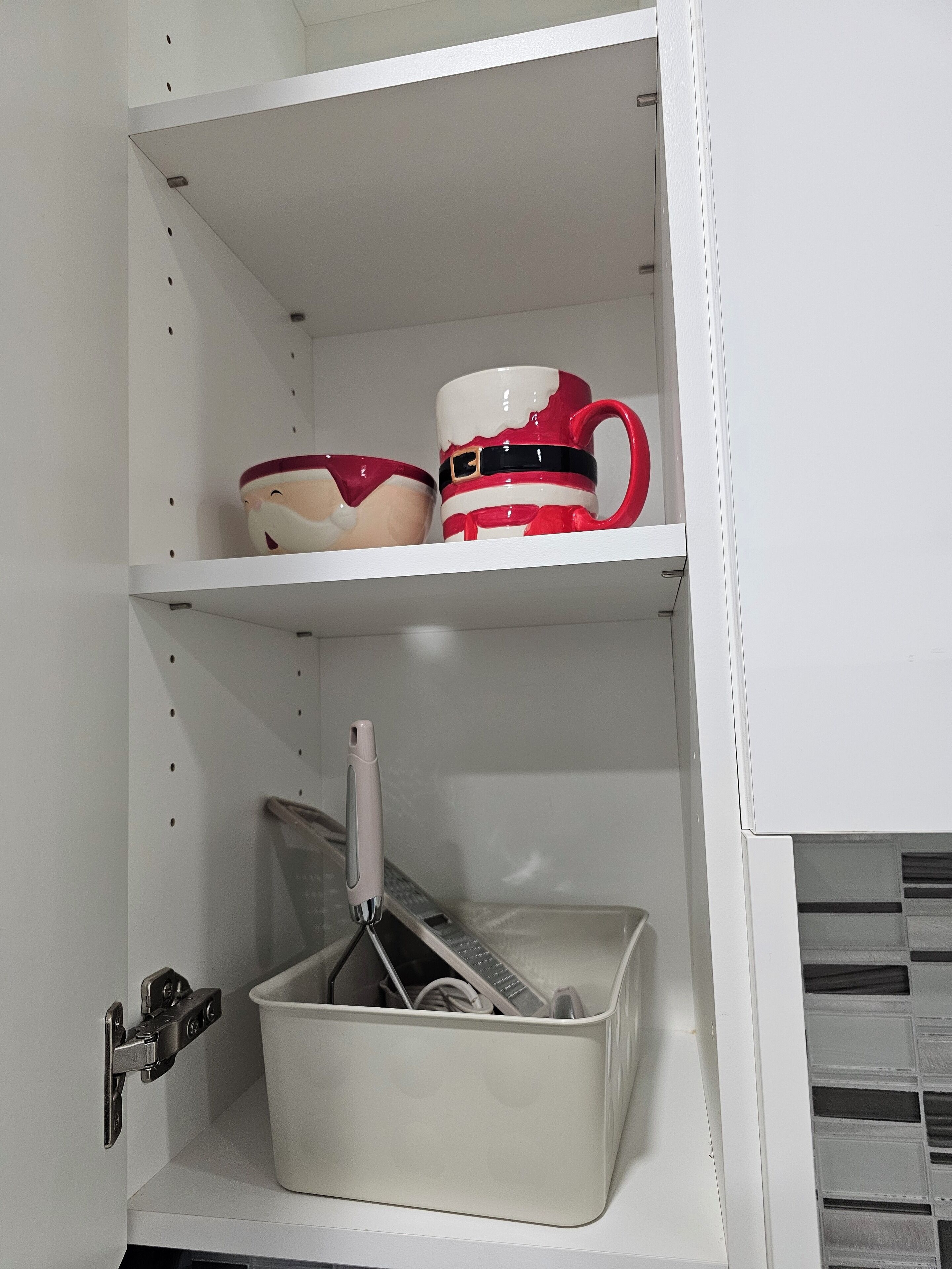A white cabinet with shelves containing kitchenware and a white basket with utensils.