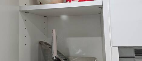 A white cabinet with shelves containing kitchenware and a white basket with utensils.