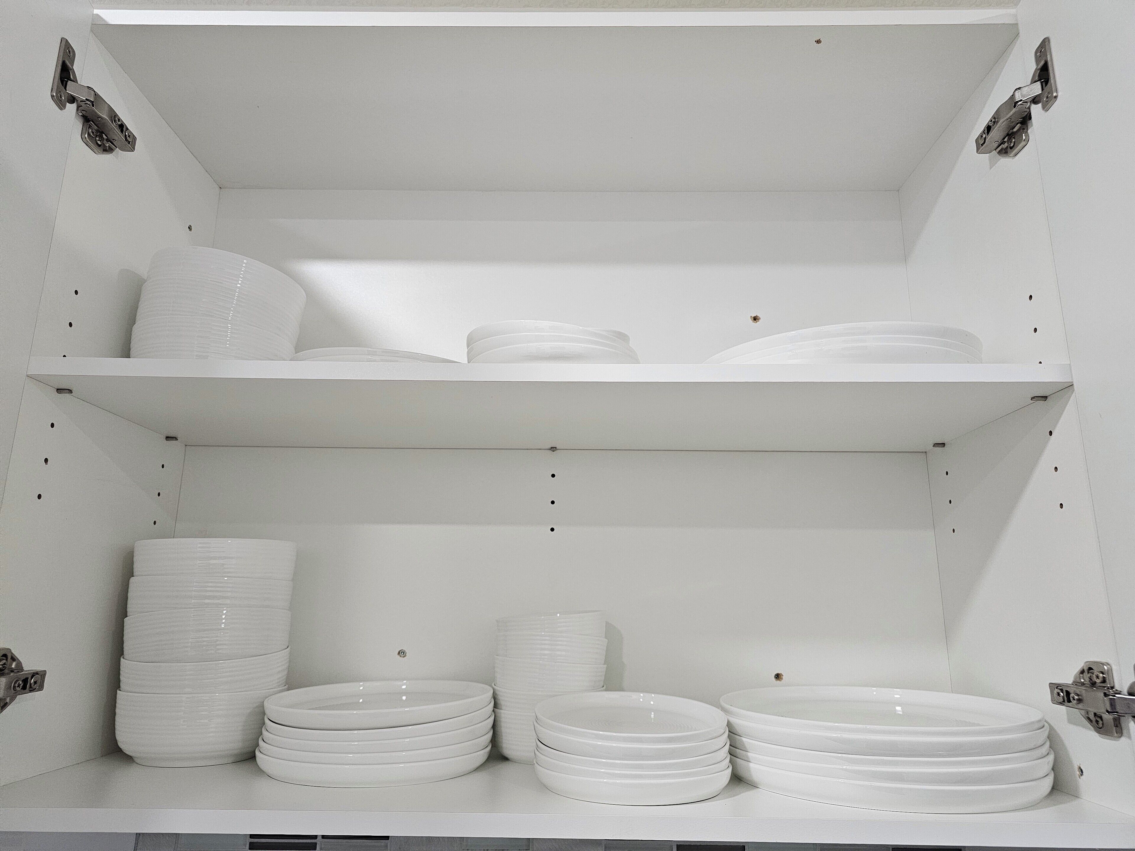 Un meuble d’étagère blanc, avec plusieurs assiettes et bols blancs.