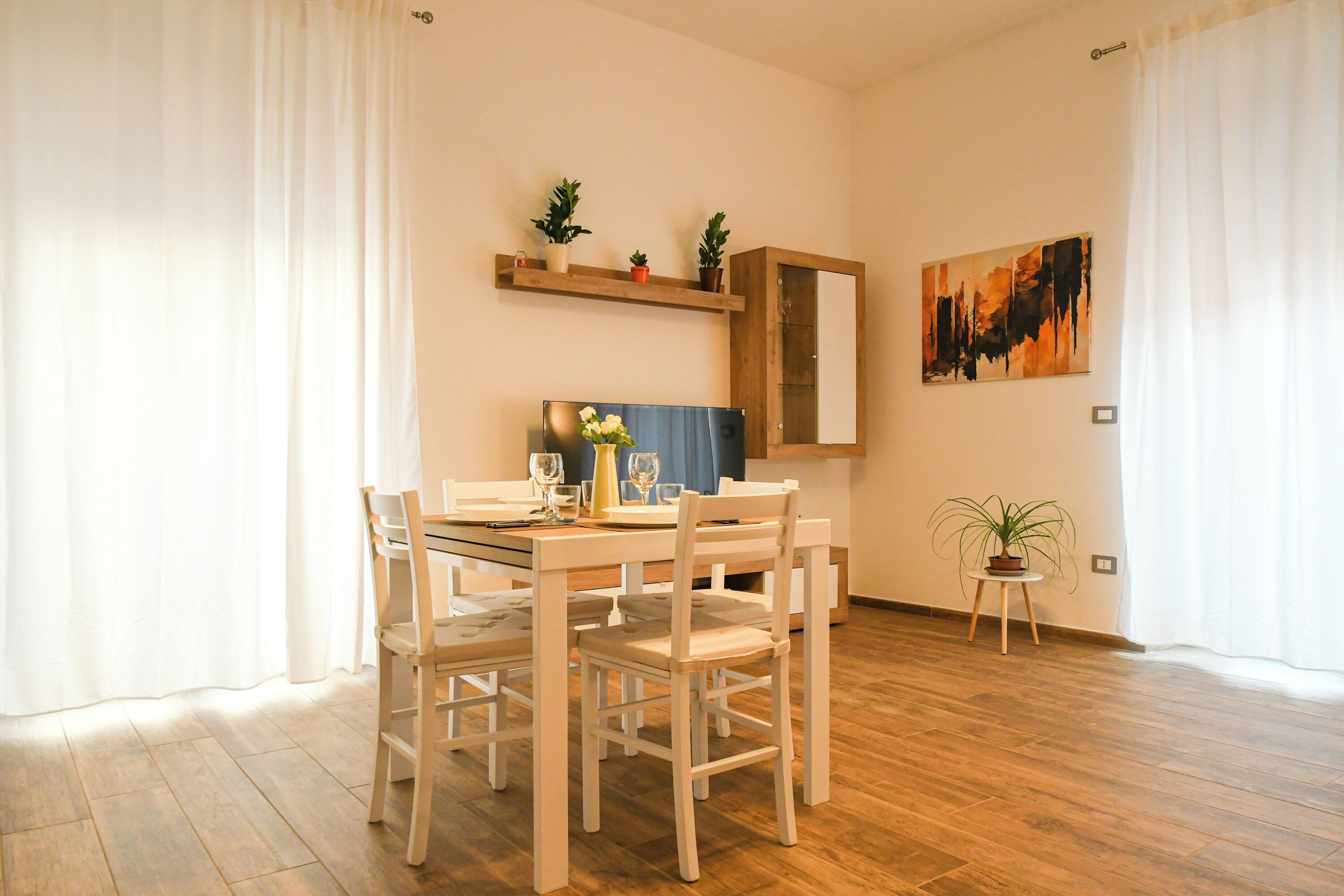 Un coin repas avec une table et des chaises en bois, une petite plante en pot et un tableau accroché au mur.