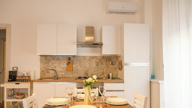 A modern kitchen with white cabinets, a granite countertop, and a dining area set for four. - House MoniK - Apartment 1 (Brindisi)