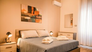 A neatly made bed with a blue blanket, two bedside lamps, and a wall-mounted air conditioner. - House MoniK - Apartment 1 (Brindisi)