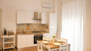 A compact kitchen with white cabinets, a gas stove, and a sink. There is a small cart with kitchen essentials and a dining table set for two. - House MoniK - Apartment 1 (Brindisi)