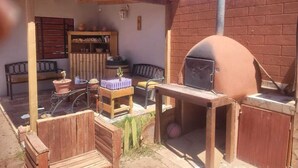 Un espace extérieur aménagé en terrasse, avec un four en briques, des meubles en bois et une petite bibliothèque.