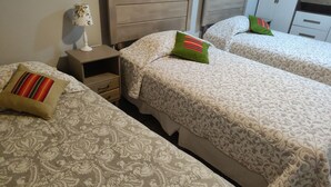 Une chambre d’hôtel avec deux lits, chacun recouvert d’une couvre-lit à motifs floraux et doté d’un oreiller à rayures. Il y a une table de chevet avec une lampe et un tiroir.
