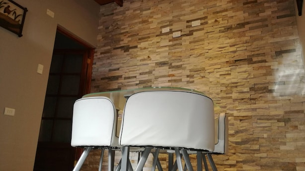 Une pièce avec un mur en pierre et une table en verre, ainsi que des chaises.