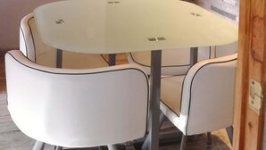 Un coin repas avec une table ronde et quatre chaises, un plafond en bois, un mur en pierre et une porte avec des panneaux de verre.