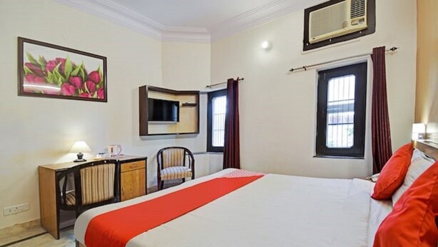 A hotel room with a large bed, a desk with a chair, a mirror, and a window with curtains.