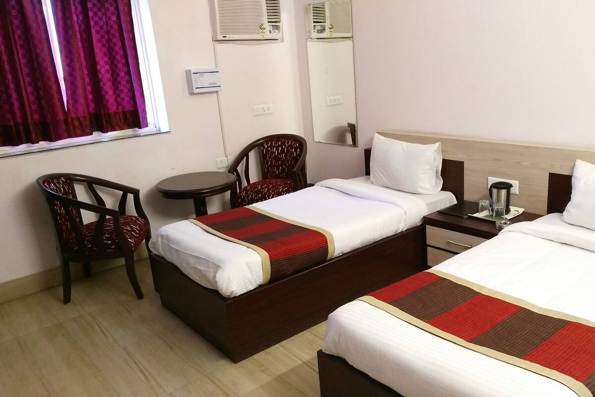A hotel room with two beds, a small table, two chairs, a heater, and a window with curtains.