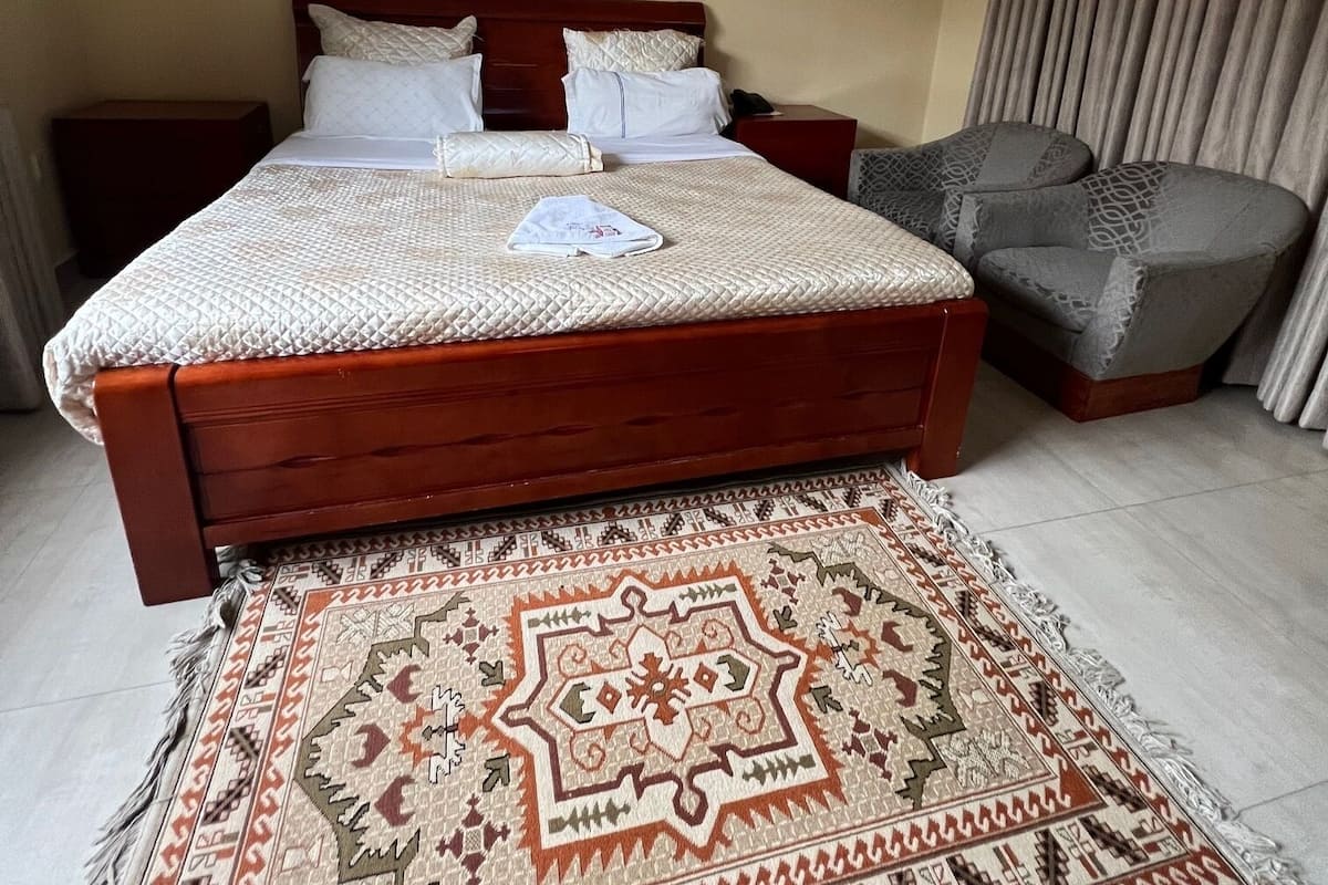 A bedroom with a large bed, a bedside table, a chair, and a patterned rug.