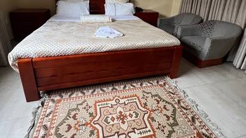 A bedroom with a large bed, a bedside table, a chair, and a patterned rug.