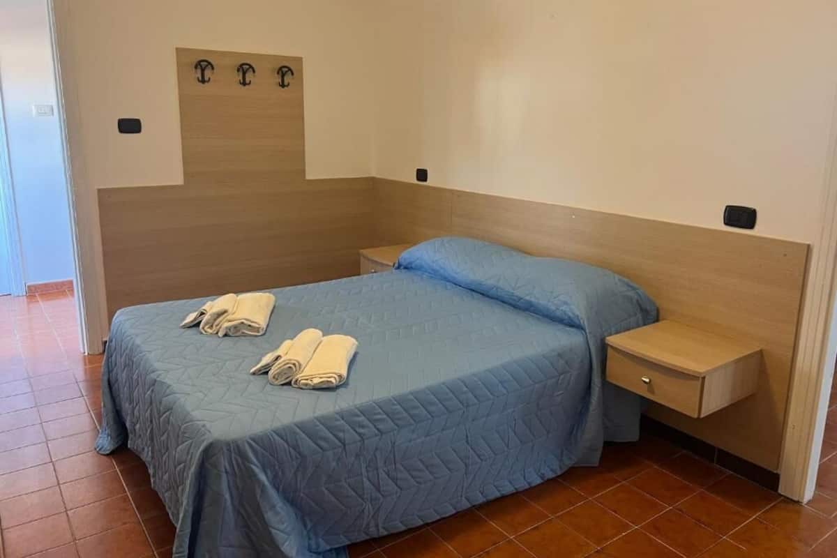 A bedroom with a bed, a nightstand, and a wall-mounted shelf.