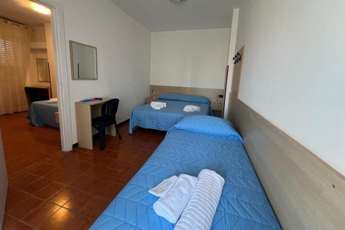 A small, clean room with two beds, a desk, and a chair.
