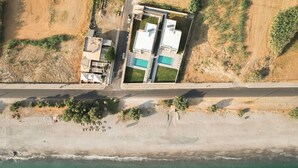 An aerial view of a coastal property with a swimming pool, a road, and a beach. - Gemini Villas | Villa Siesta (Μάλεμε)