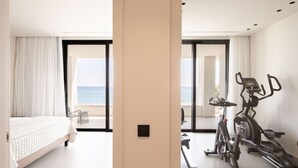 A modern hotel room with a bed, exercise equipment, and a balcony with a view of the sea. - Gemini Villas | Villa Siesta (Μάλεμε)