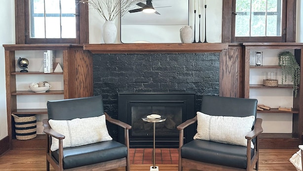 A living room with two dark leather armchairs, a small round table, a fireplace, and wooden shelves with decorative items. - Bricks - Main floor 2 bed/bath home, 2 car garage 3 blocks from Mayo Clinic! (Rochester)