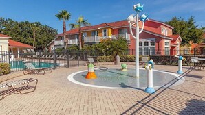 Ein Poolbereich mit Liegestühlen, einem Wasserspiel und einem Gebäude mit Balkonen im Hintergrund.