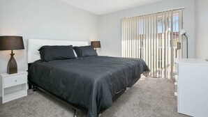Ein Schlafzimmer mit einem großen Bett, zwei Nachttischen mit Lampen, einer weißen Kommode und einem Fenster mit Jalousien.