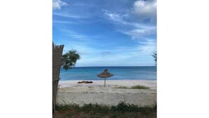 A beach with a thatched umbrella and a wooden fence. - A villa on the waterfront (Kerkouane)