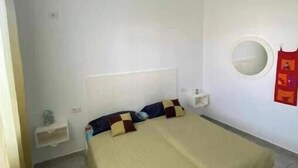 A bedroom with a bed, a bedside table, a nightstand, a wall-mounted round mirror, and a small shelf. - A villa on the waterfront (Kerkouane)