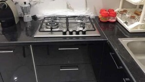 A kitchen with a gas stove, black cabinets, and a marble backsplash. - Appartement Kelibia (Kerkouane)