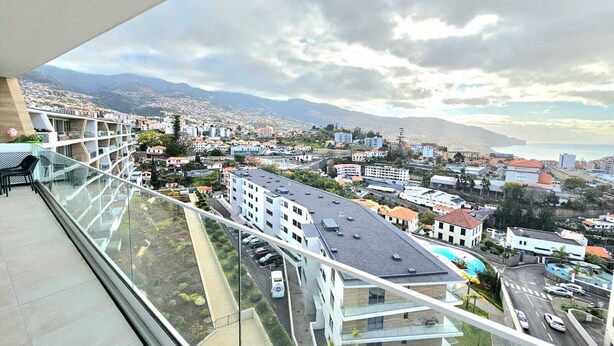 A high-rise building with a balcony overlooking a cityscape, including roads and distant mountains.