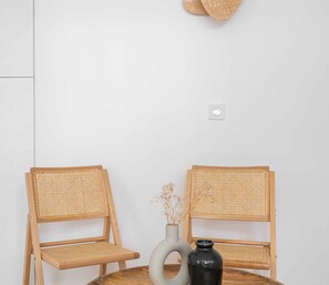 Two wicker chairs with a round table in between, a white vase with dried flowers, and a black vase.
