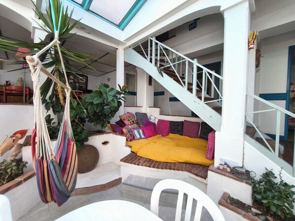 Un espace extérieur accueillant, aménagé avec un canapé et des coussins, un hamac et un escalier menant à un niveau supérieur.