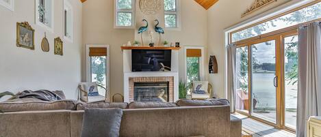 A spacious living room with a large sectional sofa, a fireplace, and a view of a lake through large sliding glass doors.