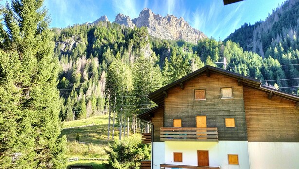 A wooden cabin with a balcony, surrounded by a forest and mountains in the background. - El Zirum-Boscoverde 3 (Rocca Pietore)