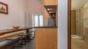 A modern kitchen with wooden cabinetry, a dining table with benches, and a shower area. - El Zirum-Boscoverde 3 (Rocca Pietore)