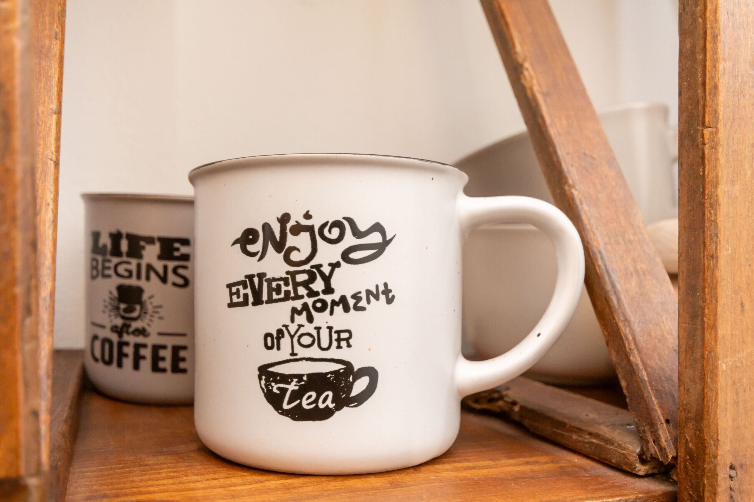 Two white mugs with black text and illustrations, placed on a wooden surface.