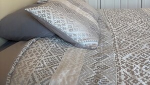 A bed with patterned bedding and pillows, a plain wall, and a white door in the background. - Beautiful 3 Bedroom condo apt near Owl's Nest golf course and wedding venue (Thornton)