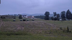 A grassy field with a few scattered trash bins and a distant view of a house with a red roof. - Beautiful 3 Bedroom condo apt near Owl's Nest golf course and wedding venue (Thornton)
