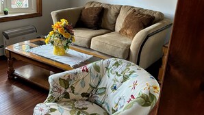 Un soggiorno con un divano beige, una poltrona con motivi floreali, un tavolino da caffè con un vaso di fiori e due quadri appesi al muro.