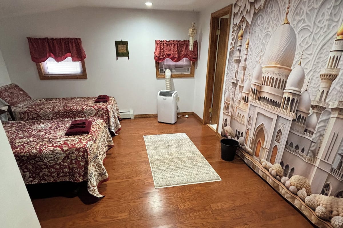 Une chambre avec deux lits, un radiateur, un tapis à motifs et une fresque murale représentant une mosquée.