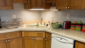 Una cucina con mobili in legno, una lavastoviglie bianca, un lavello e un piano di lavoro con diversi oggetti da cucina.