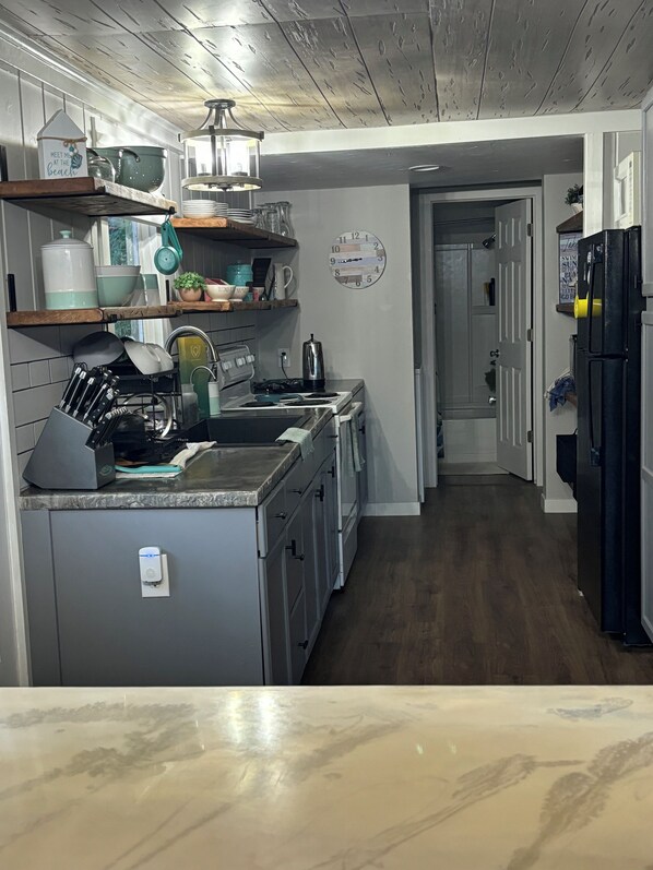 A kitchen with a central island, a stove, and a refrigerator. There are shelves above the counter and a clock on the wall.