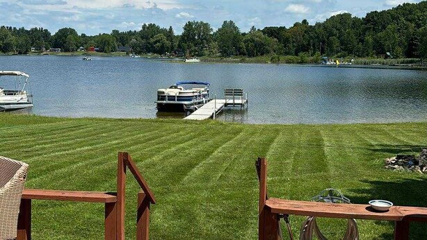 Une terrasse en bois offrant une vue sur un lac, des bateaux et une zone herbeuse.