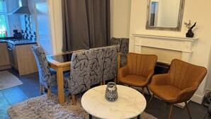 Una sala de estar con comedor, chimenea y cocina visible a través de una puerta abierta.