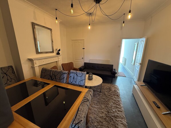 A modern living room with a glass coffee table, a sofa, a TV, and a fireplace.