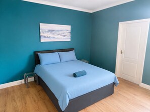 A bedroom with a bed, a nightstand, a wall-mounted painting, and a door.