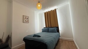Un dormitorio con cama, una lámpara en el techo, una ventana con cortinas y un cuadro colgado en la pared.